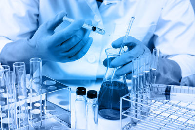 Midsection of scientist wearing gloves holding conical flask in laboratory