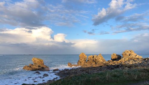 Scenic view of sea and rocks against cloudy sky