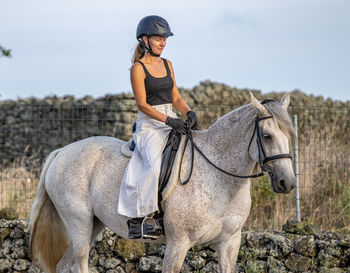 White lusitano mare, female dressage rider, outdoors on sand.