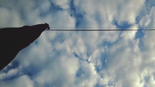 Low angle view of hand holding cables against sky