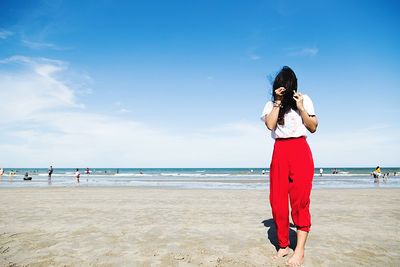 Woman with hair covering face standing at beach against sky