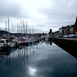 Boats moored at harbor against sky in city