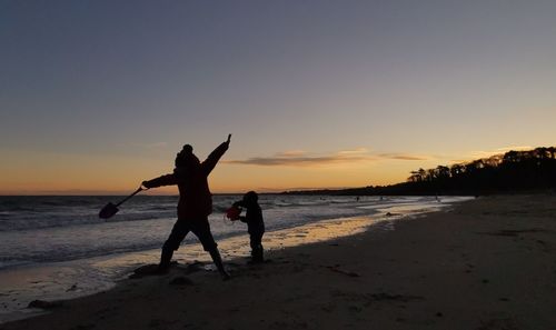 Silhouette people at beach against sky during sunset