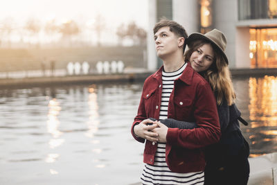 Young couple embracing by lake in city during sunset