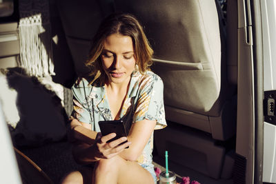 Blonde pretty woman into a minivan using her smartphone with sun getting into van