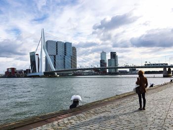 Rear view full length of woman by river looking at erasmus bridge in city