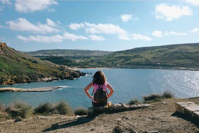 Rear view of woman sitting on cliff against lake