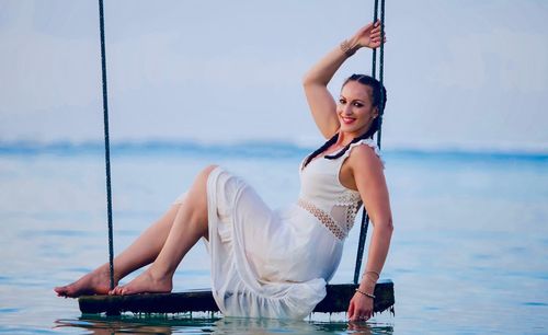 Young woman sitting in sea against sky