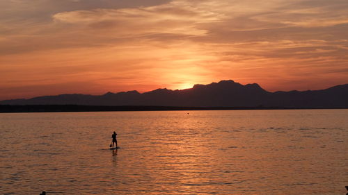 Silhouette person on shore against orange sky