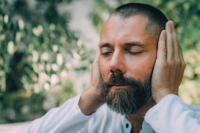 Man sitting with his eyes closed and doing a reiki auto treatment, holding hands on ears.