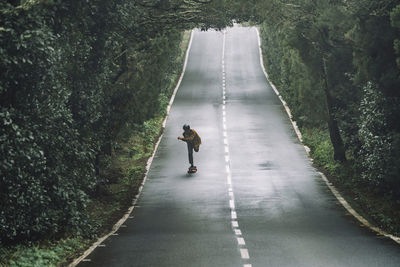 Rear view of man walking on road amidst trees