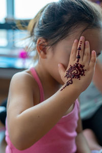 Portrait of henna ornaments on little girl's hand covering face.