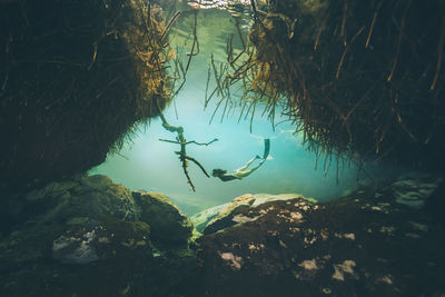 Woman swimming underwater by rock formation 