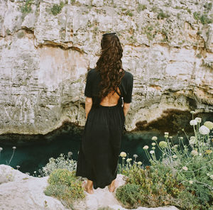 Rear view of woman standing on cliff by river