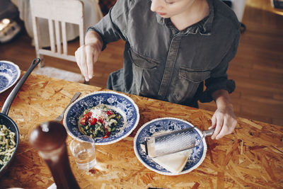 High angle view of woman sprinkling cheese on pasta in plate at home