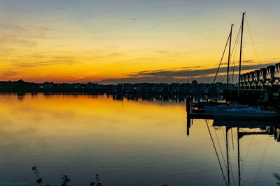 Sailboats moored at harbor against sky during sunset