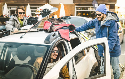 Happy male friends with ski and snowboard on car