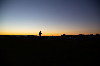 Silhouette man standing on shore against sky during sunset