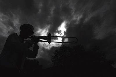 Low angle view of silhouette man playing trumpet against cloudy sky