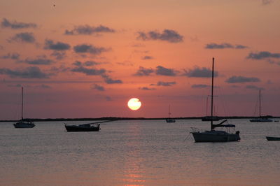 Sailboats moored on sea against sky during sunset