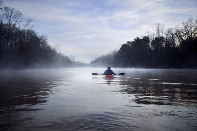 Rear view of man kayaking on chattahoochee river amidst bare trees against sky