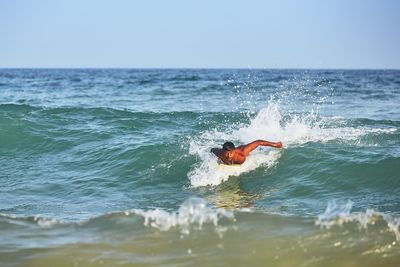 Man surfing on wave in sea against sky