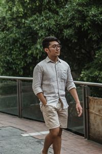 Young man standing by railing against trees