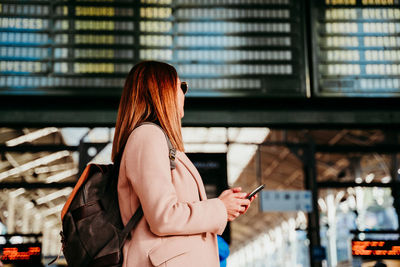 Side view of woman wearing backpack standing on railroad station