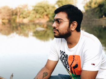 Young man wearing sunglasses sitting by water