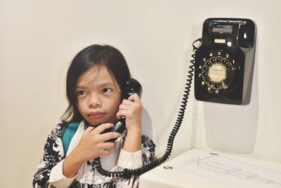 Portrait of a smiling girl holding mobile phone against wall