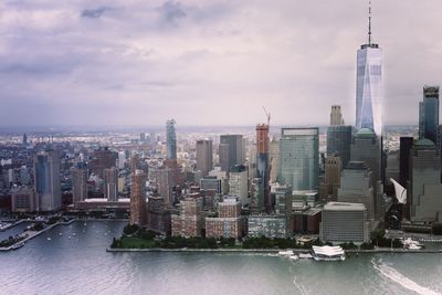 One world trade center by hudson river against cloudy sky