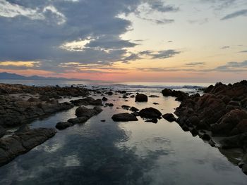 Rocks in sea against sky during sunset