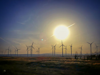 Wind turbines on field against sky at sunset