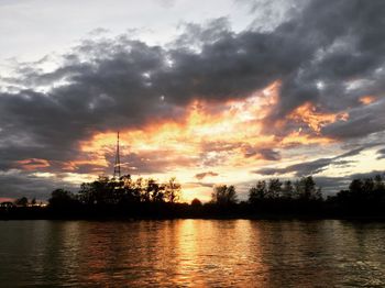 Scenic view of lake against dramatic sky during sunset