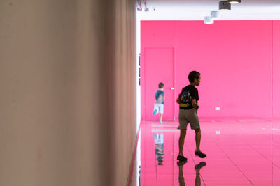 Full length of woman standing against pink wall