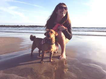 Portrait of young woman with dog on beach against sky