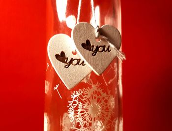 Close-up of text on heart shape with bottle hanging against red background