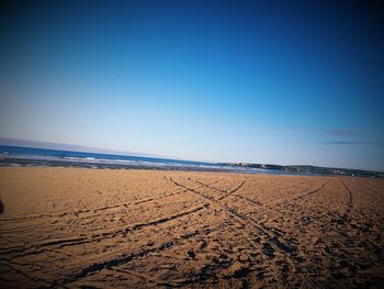 Tire tracks at beach against clear blue sky