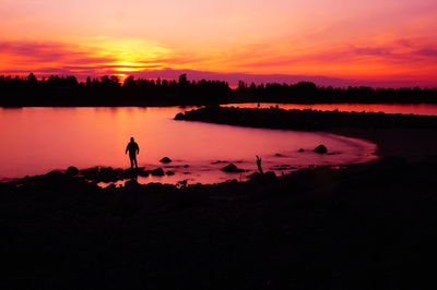 Silhouette people on lake against orange sky