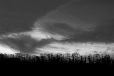 Silhouette of trees on field against cloudy sky