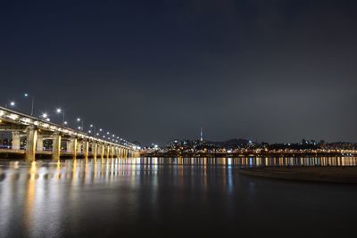 Illuminated bridge over river against sky at night