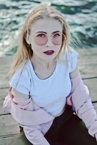 Portrait of young woman sitting on pier by sea