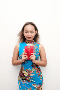 Portrait of smiling young woman holding envelope against white background