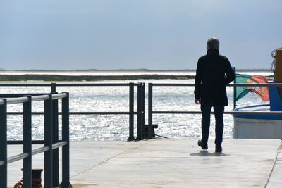 Rear view of man walking on pier over sea against clear sky