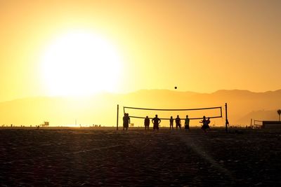 Silhouette people on beach against clear sky during sunset