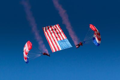 Low angle view of men paragliding with american flag in clear blue sky