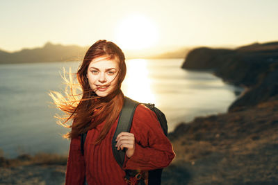 Portrait of woman standing by sea against sky during sunset