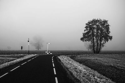 Empty road amidst field in foggy weather