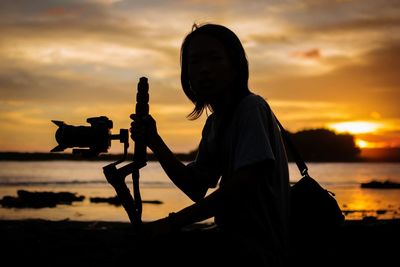 Silhouette man photographing against sky during sunset