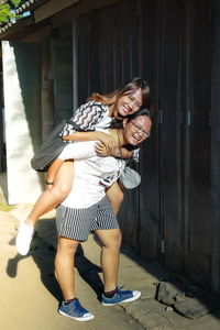 Full length portrait of smiling teenage girl giving piggyback to sister by closed shop